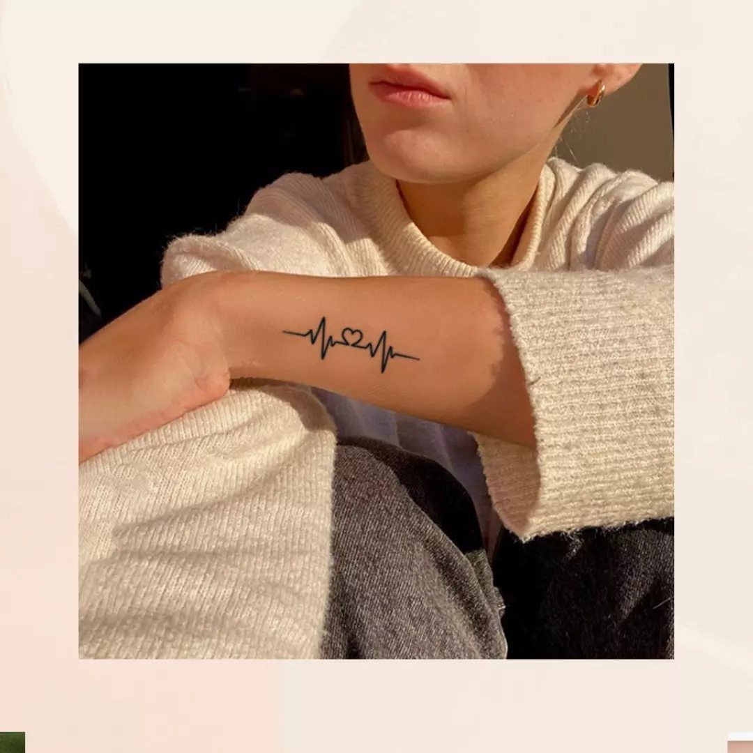 Heartbeat line tattoo with a small heart on a person's inner wrist.