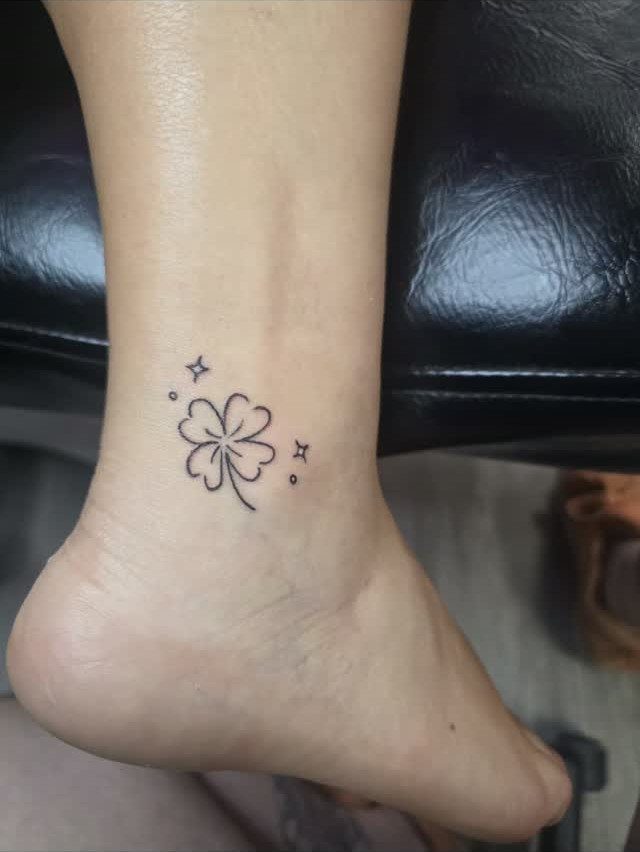 Four-leaf clover tattoo with small sparkles on a person's ankle.