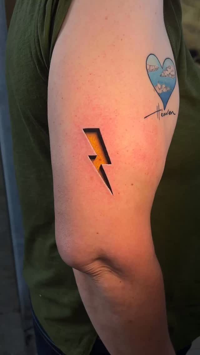 Yellow lightning bolt tattoo and a blue heart tattoo on a person's arm.