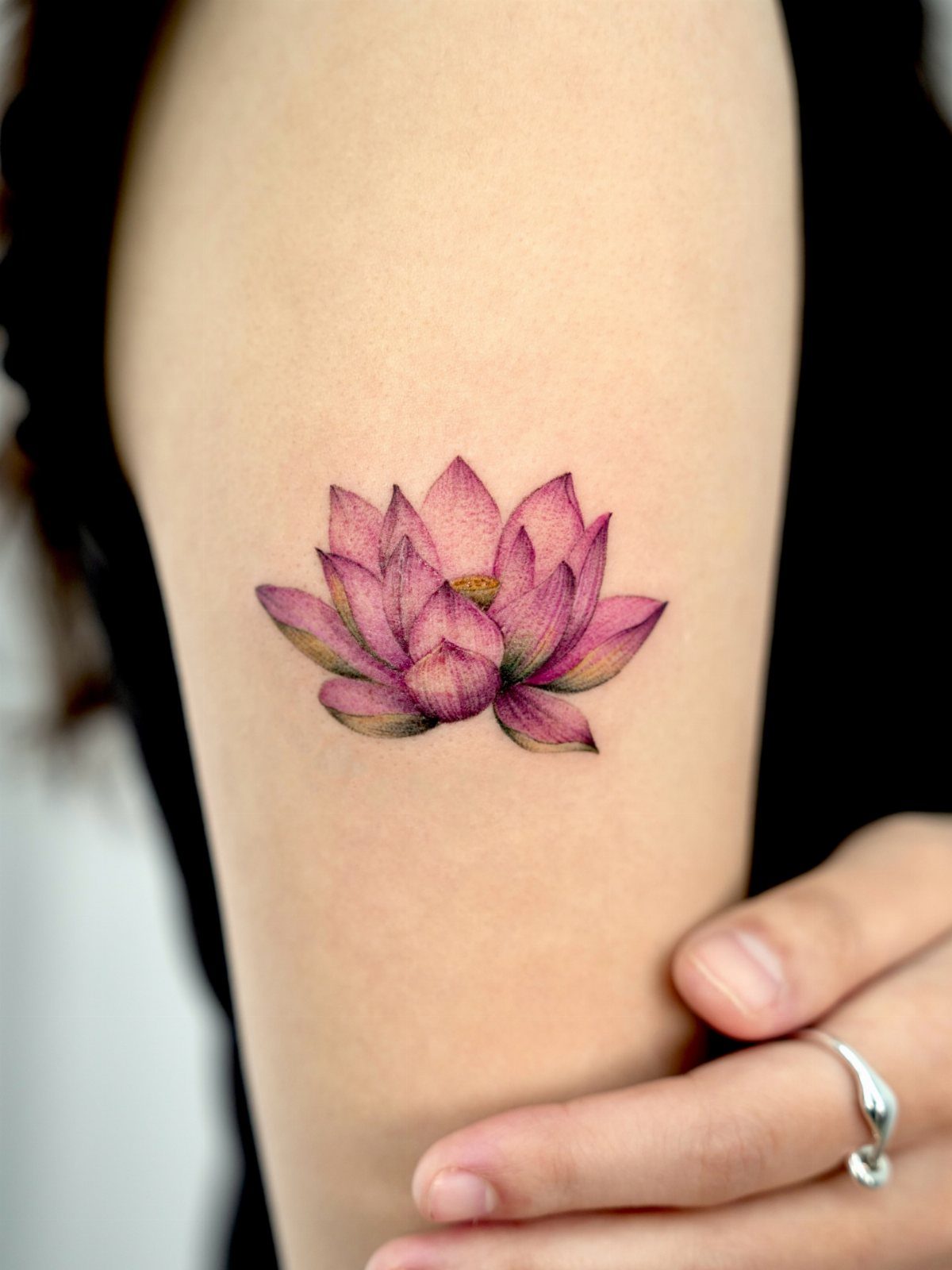 Pink and purple lotus flower tattoo on a person's upper arm.