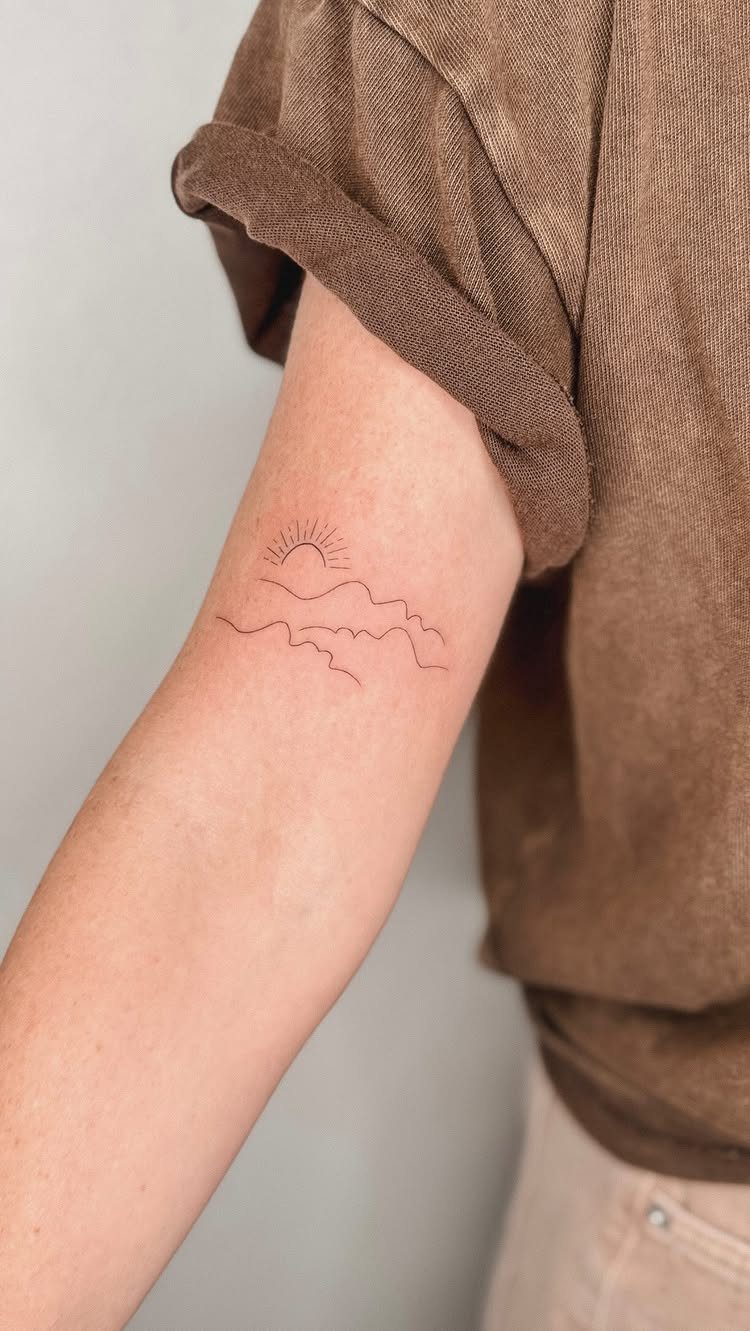 Small fine-line tattoo of mountains and a sun on a person's forearm.