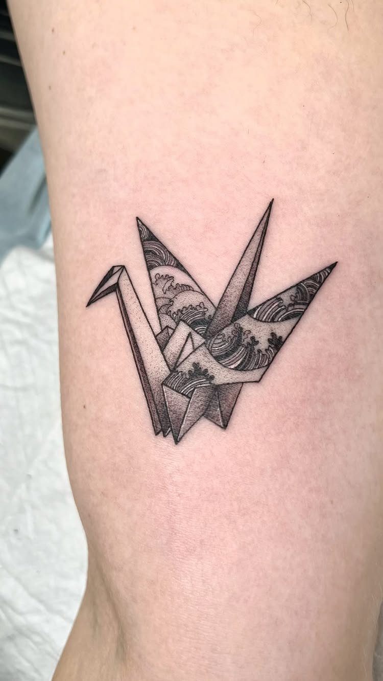 Origami paper crane tattoo with wave patterns on a person's arm.