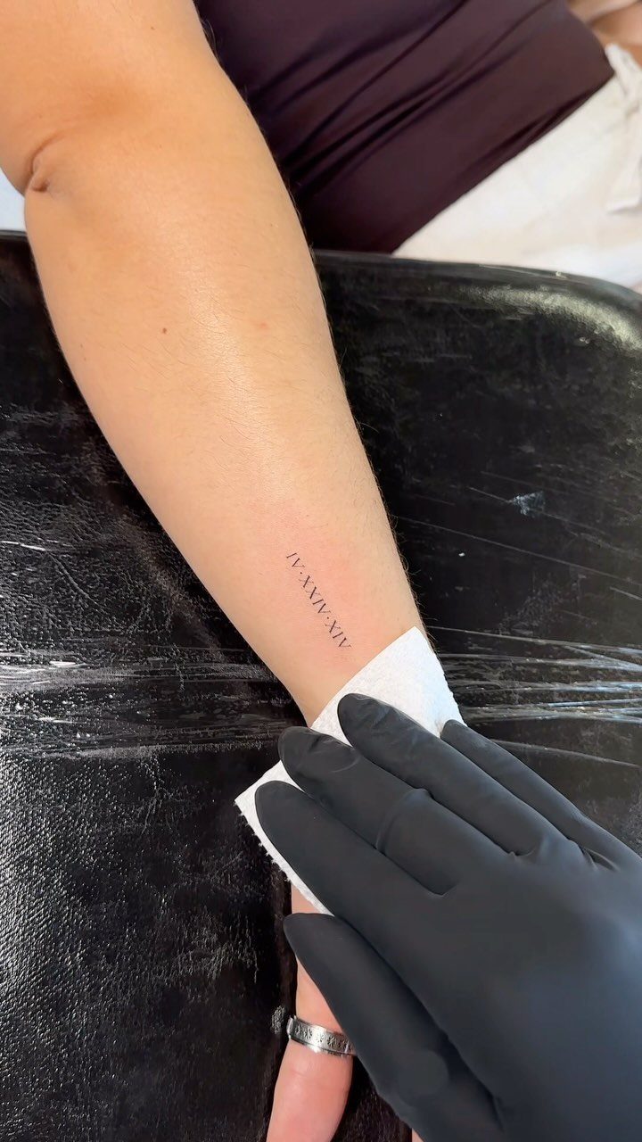 Small Roman numeral tattoo on a person's inner forearm being blotted with paper.