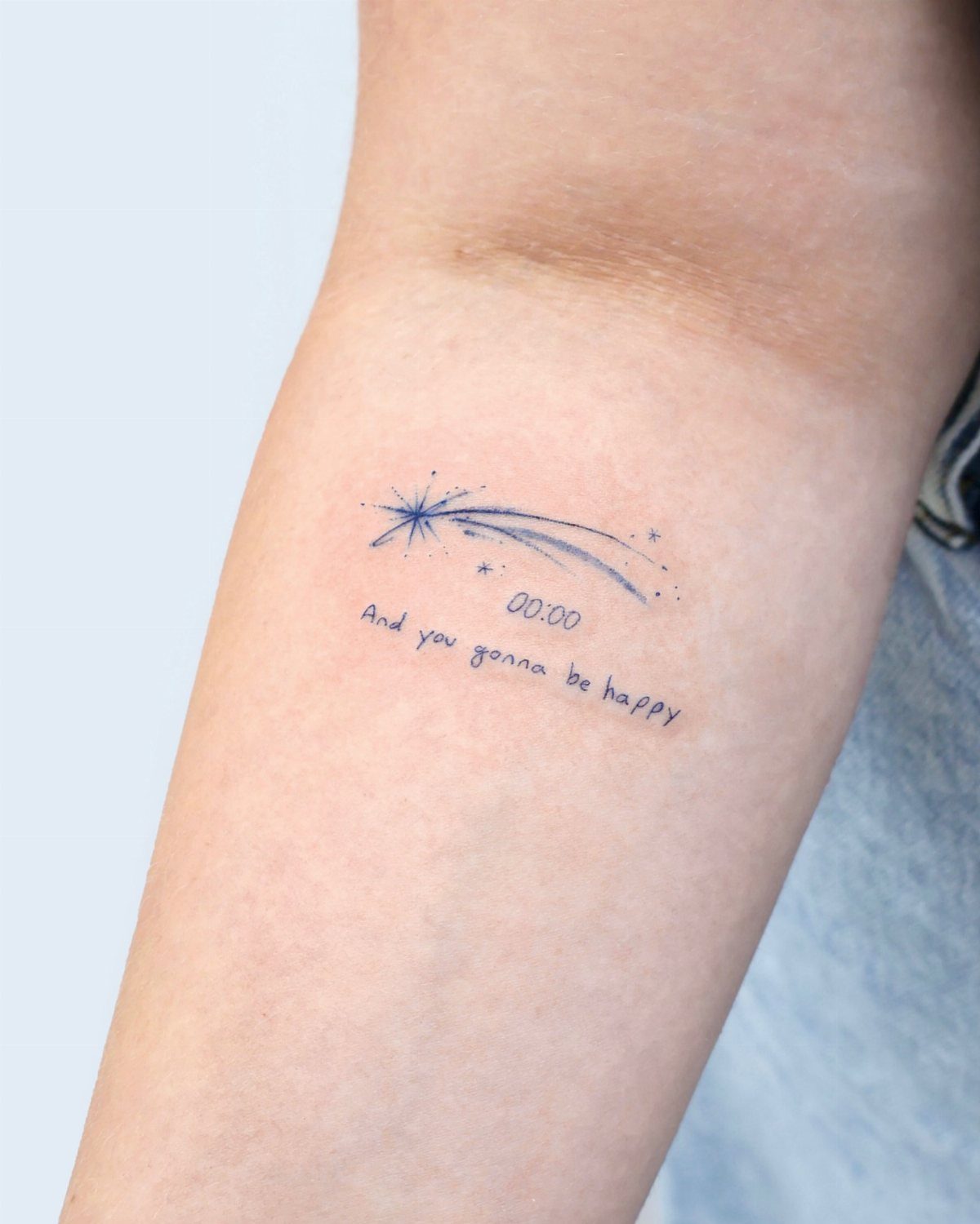 Shooting star tattoo with text and numbers on a person's inner forearm.