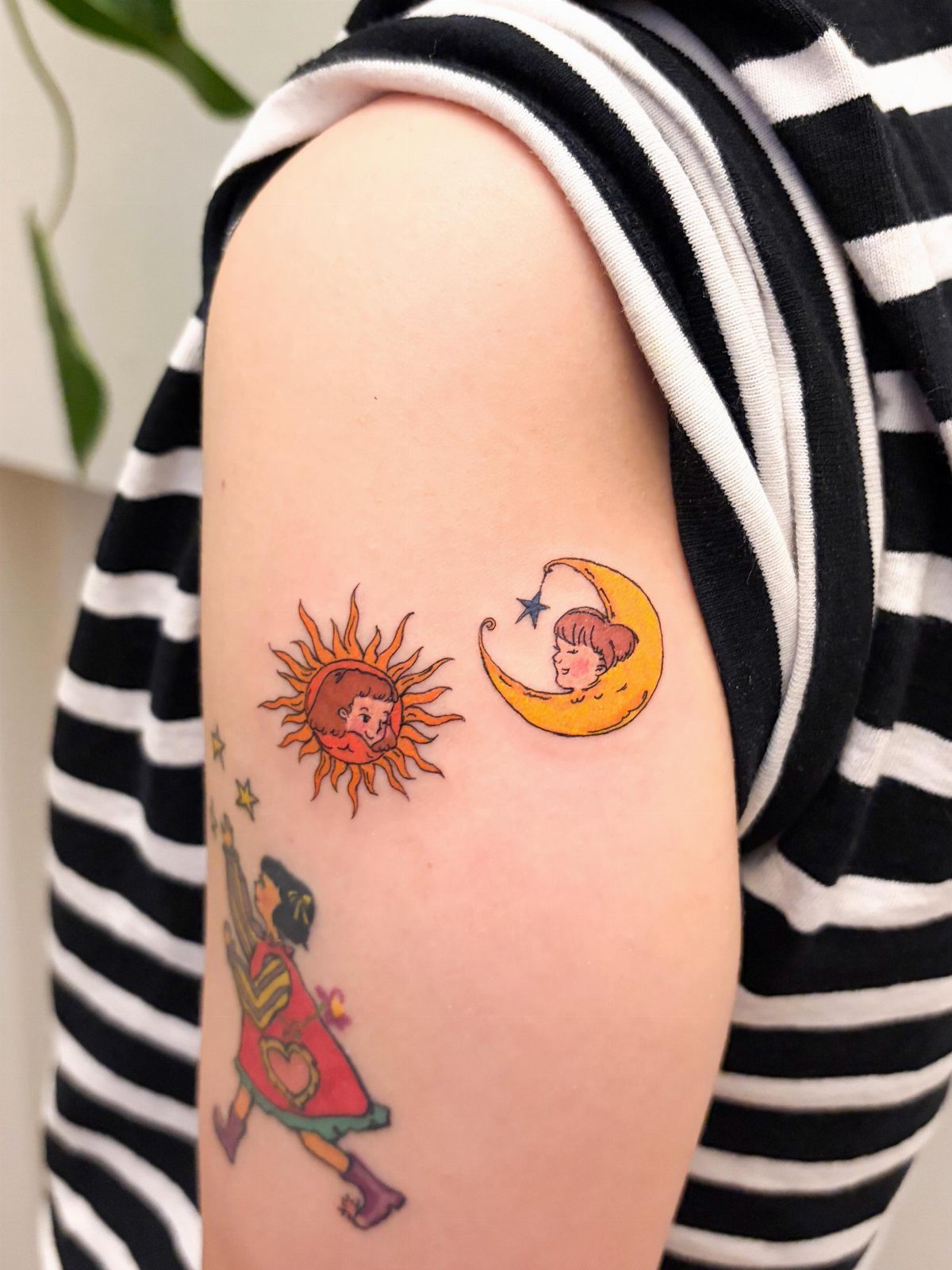 Sun and crescent moon tattoos with faces on a person's upper arm.