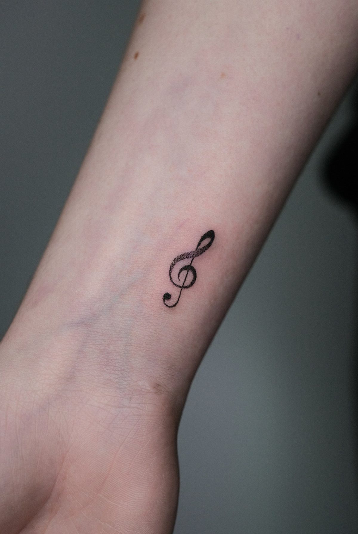 Small black treble clef tattoo on a person's inner wrist.