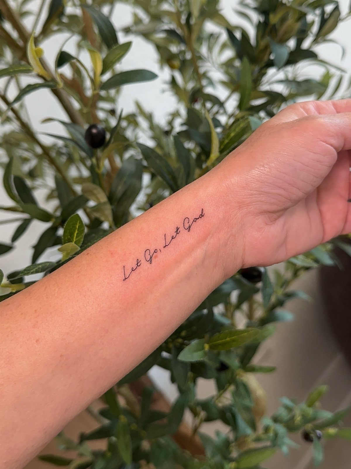 Cursive black ink tattoo on a wrist reading Let Go, Let God.