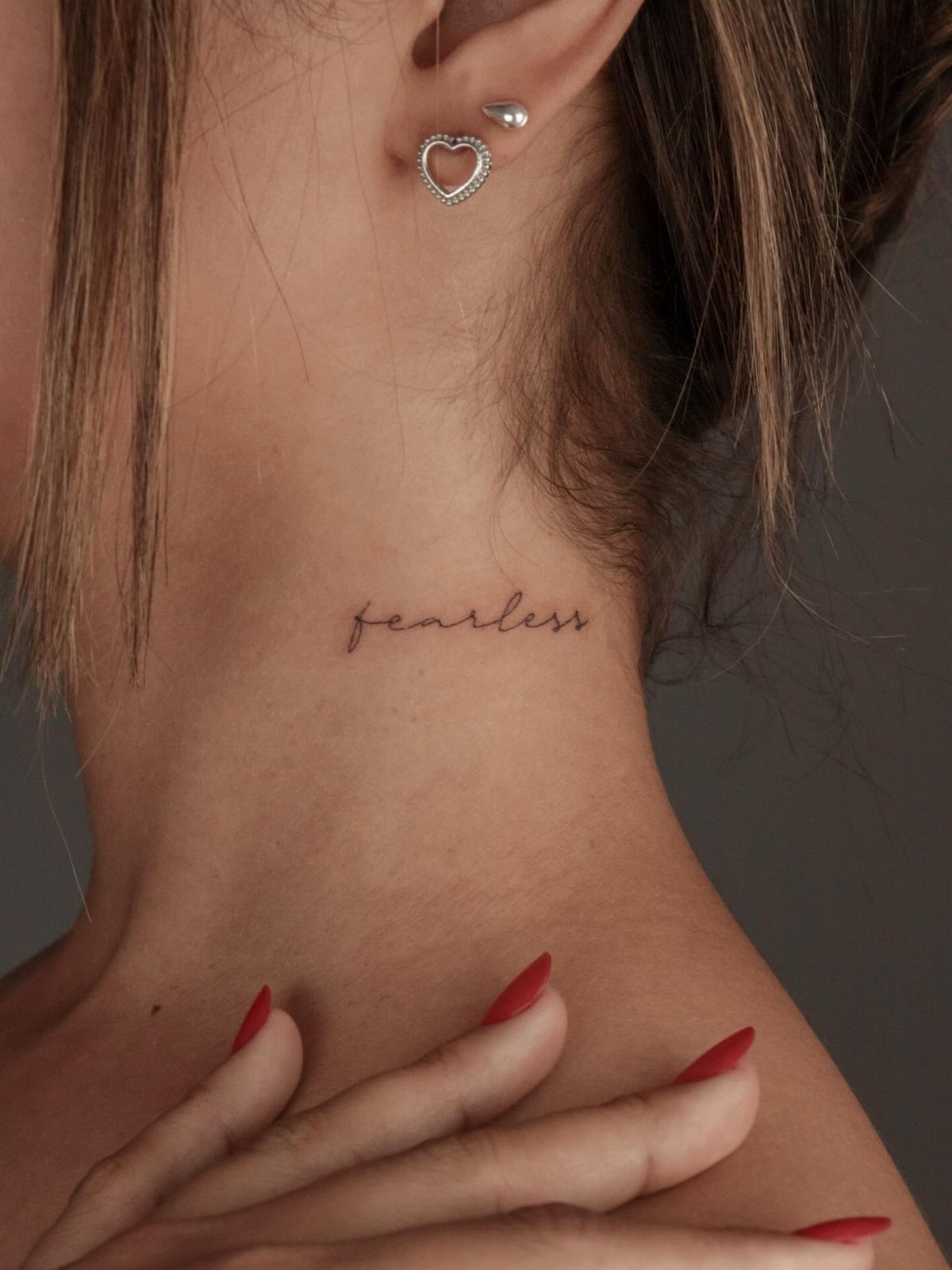 Cursive fearless tattoo on the back of a person's neck with red nails.