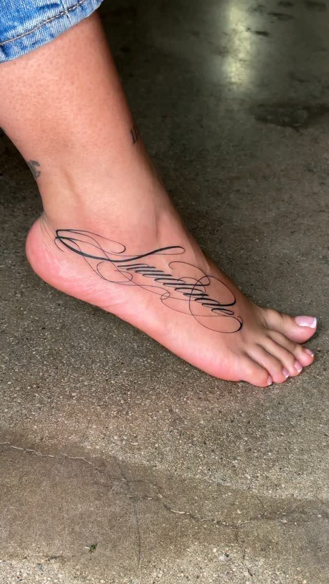 Cursive word tattoo in black ink on the top of a person's foot.