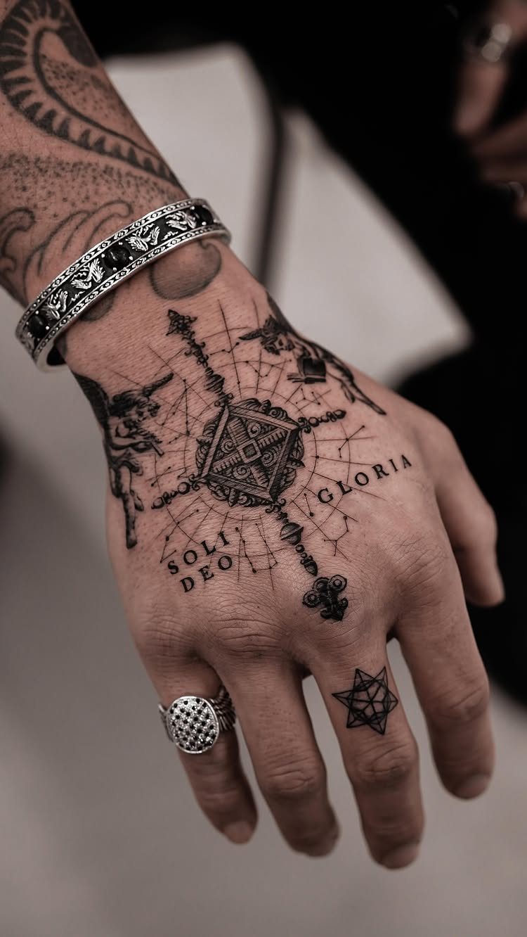 Tattooed hand featuring a geometric compass and the Latin words Soli Deo Gloria.