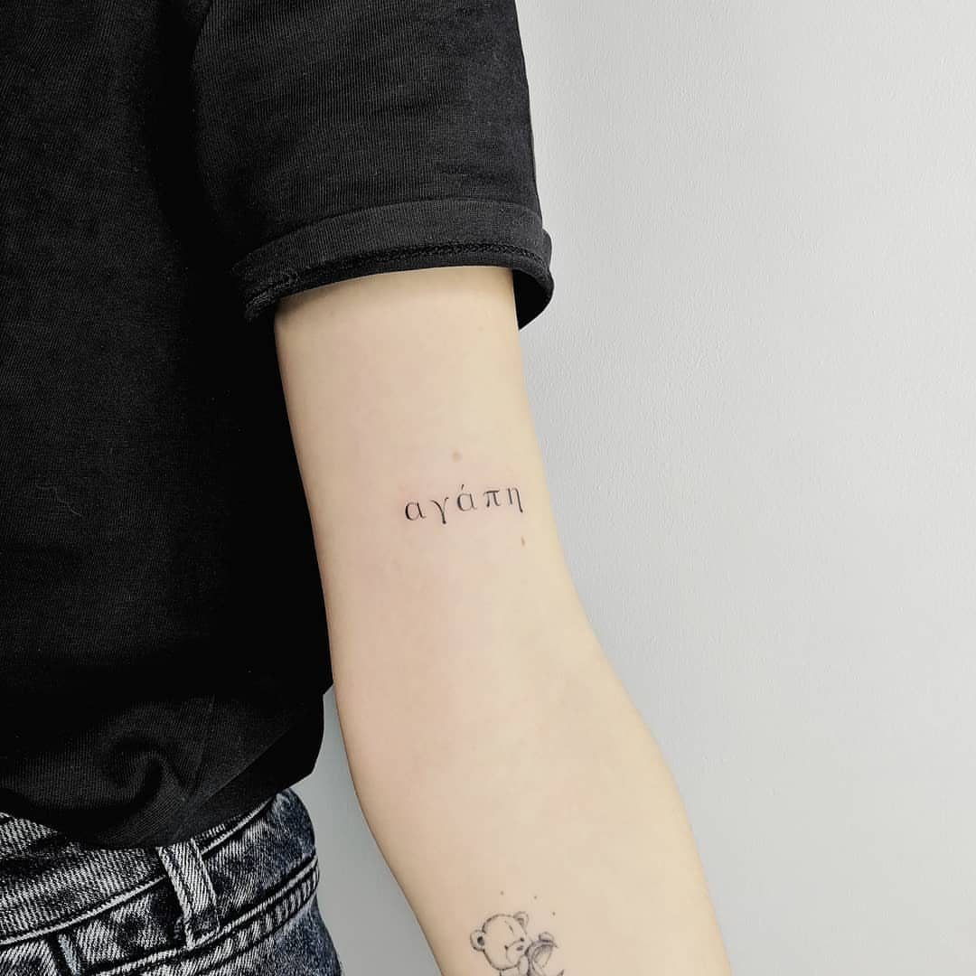 Inner forearm with a small black Greek word tattoo and a tiny drawing.