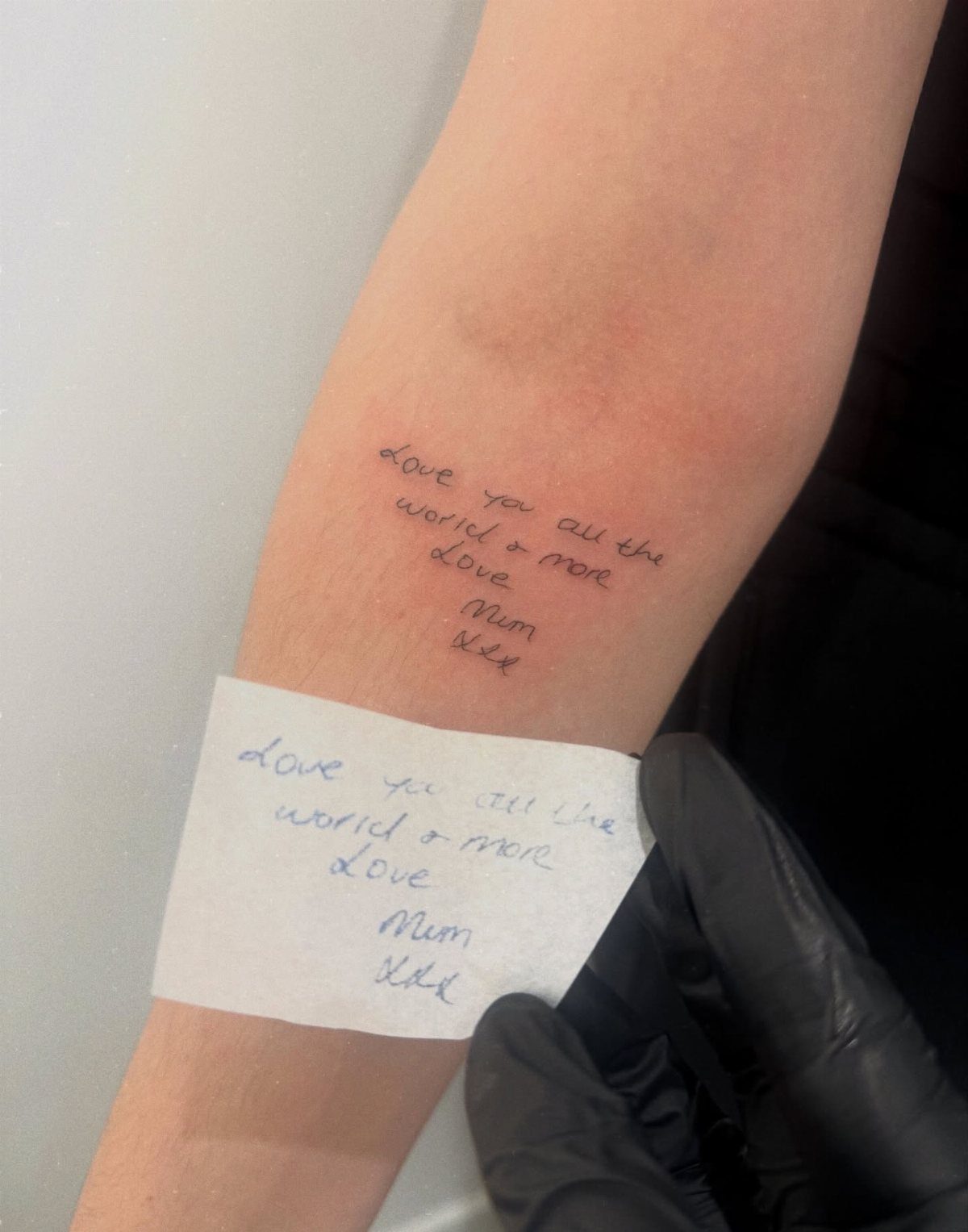 Handwritten tattoo on a forearm with the original reference note held below it