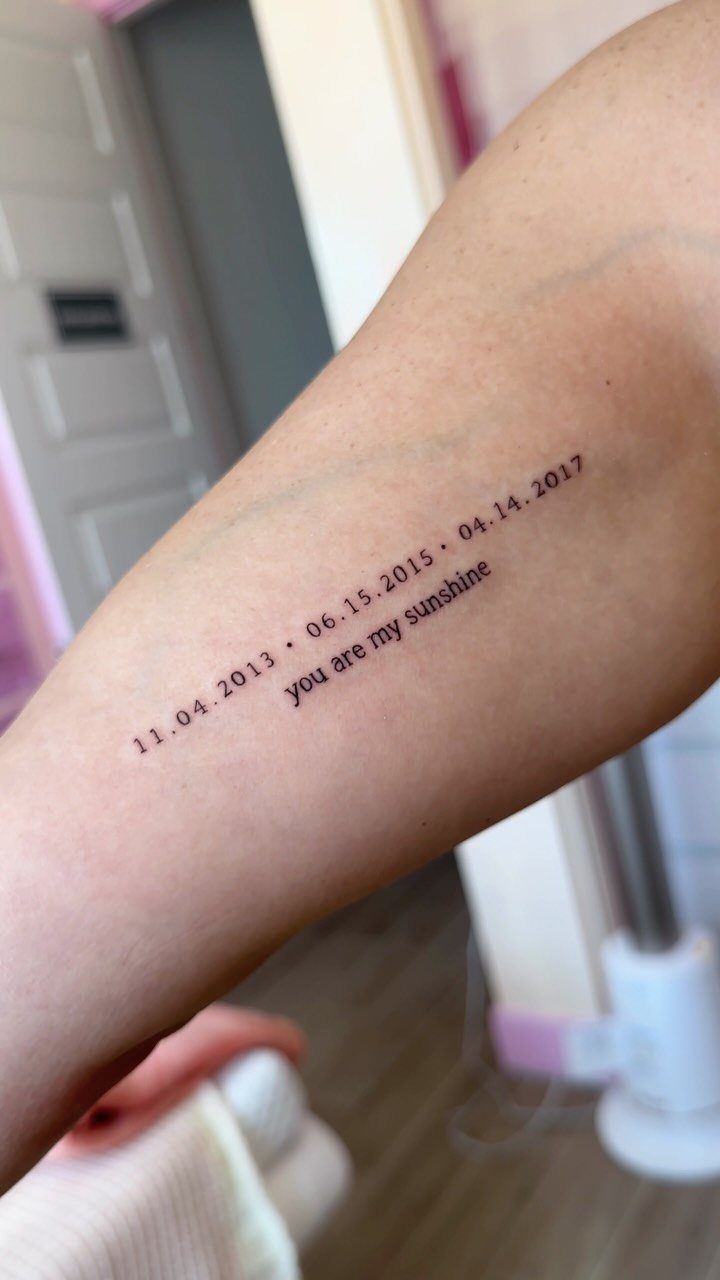 Forearm tattoo with three specific dates and the phrase you are my sunshine