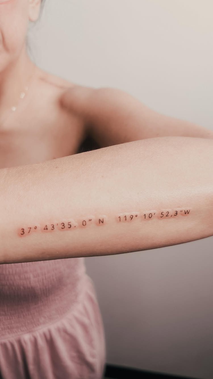 Geographical coordinates tattooed in red ink on a person's inner forearm.