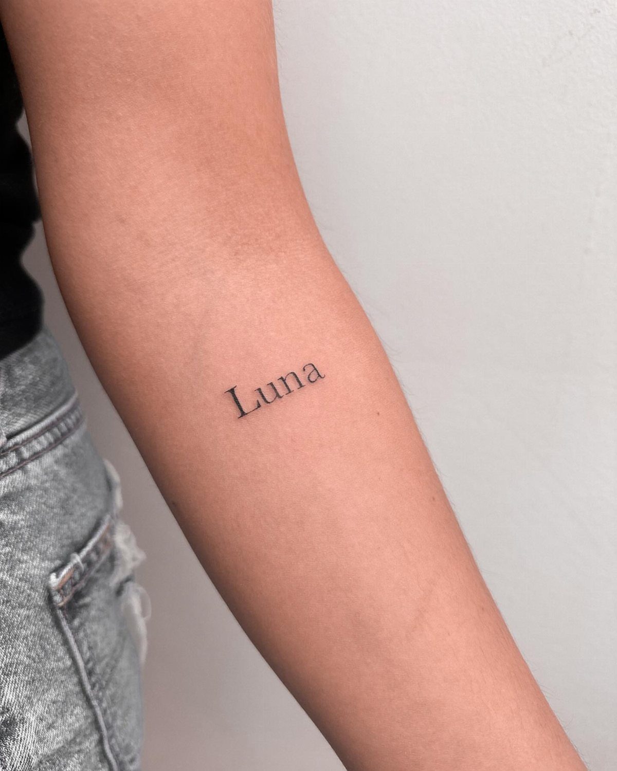 Forearm with a small black ink tattoo of the word Luna in serif font