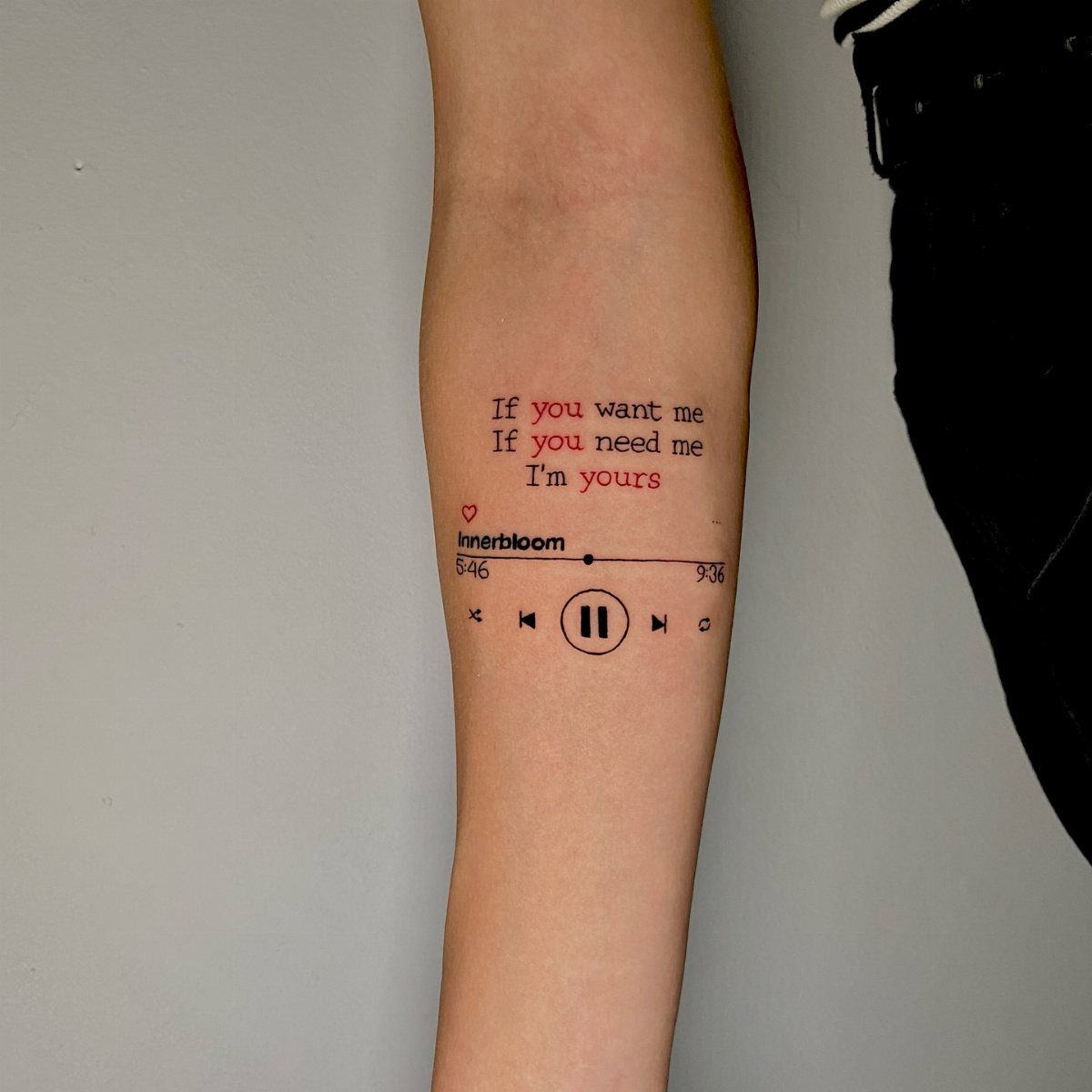 Forearm tattoo of song lyrics and a music player interface with red and black ink