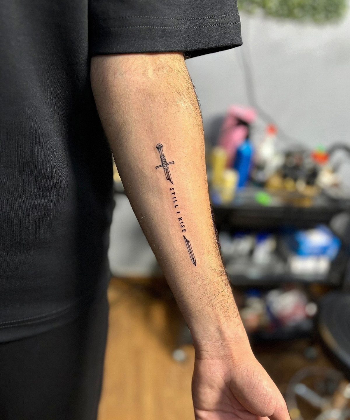 Forearm tattoo of a sword with the words Still I Rise written vertically.