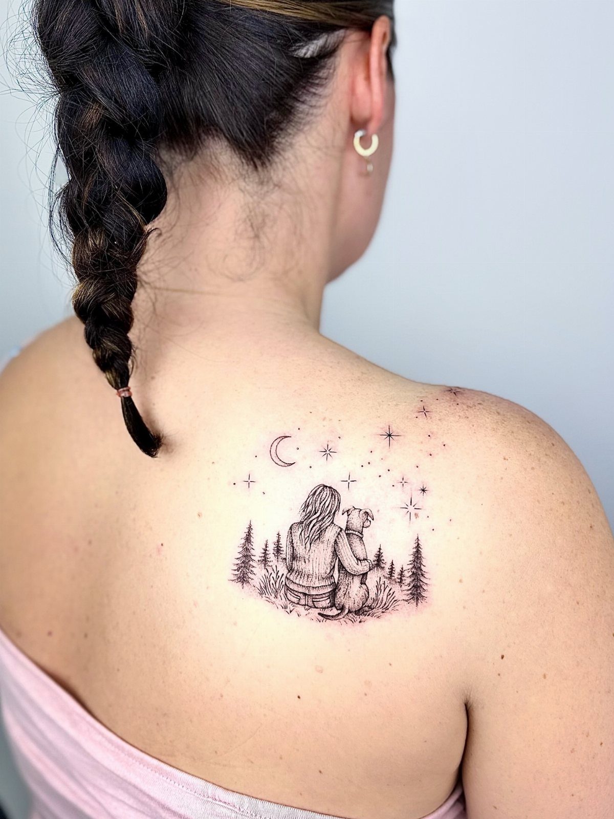 Tattoo on a woman's back depicting a person and dog viewing a forest.