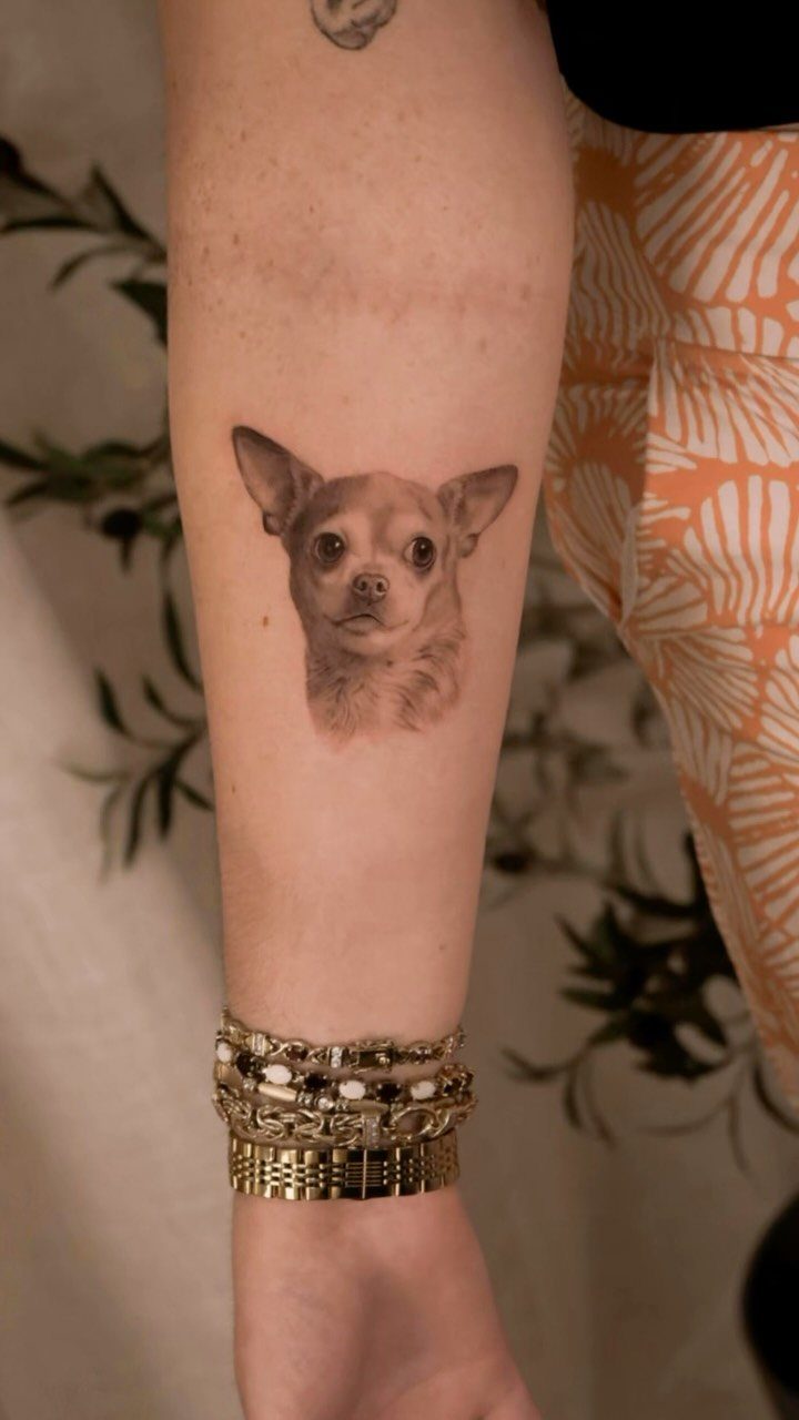 Realistic dog portrait tattoo on a forearm with gold and silver bracelets.