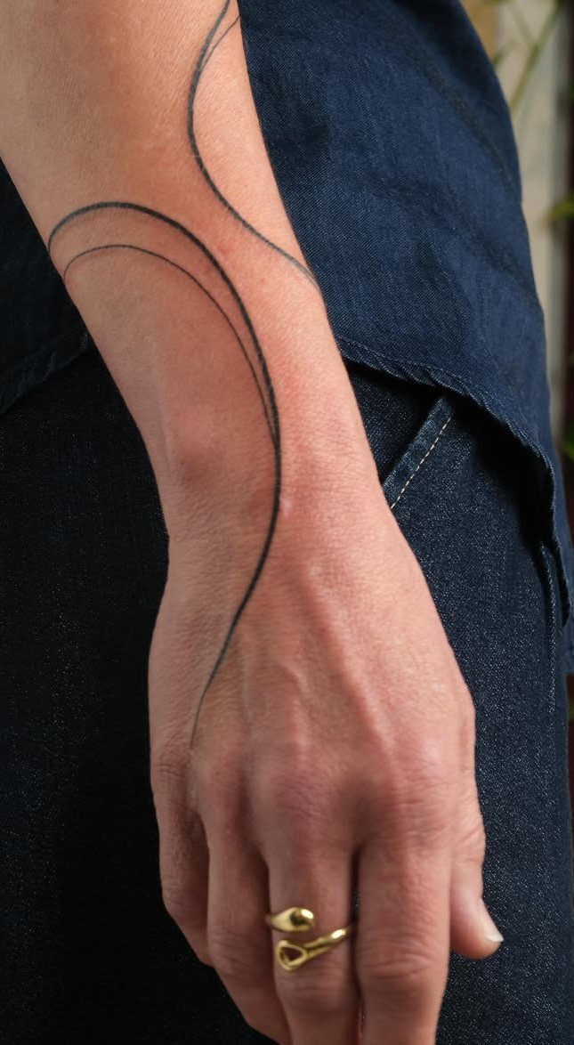 Minimalist tattoo of flowing abstract black lines on a person's wrist and hand.