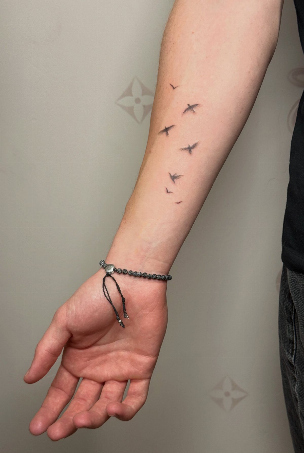 Forearm with a minimalist tattoo of small black bird silhouettes flying in sequence.