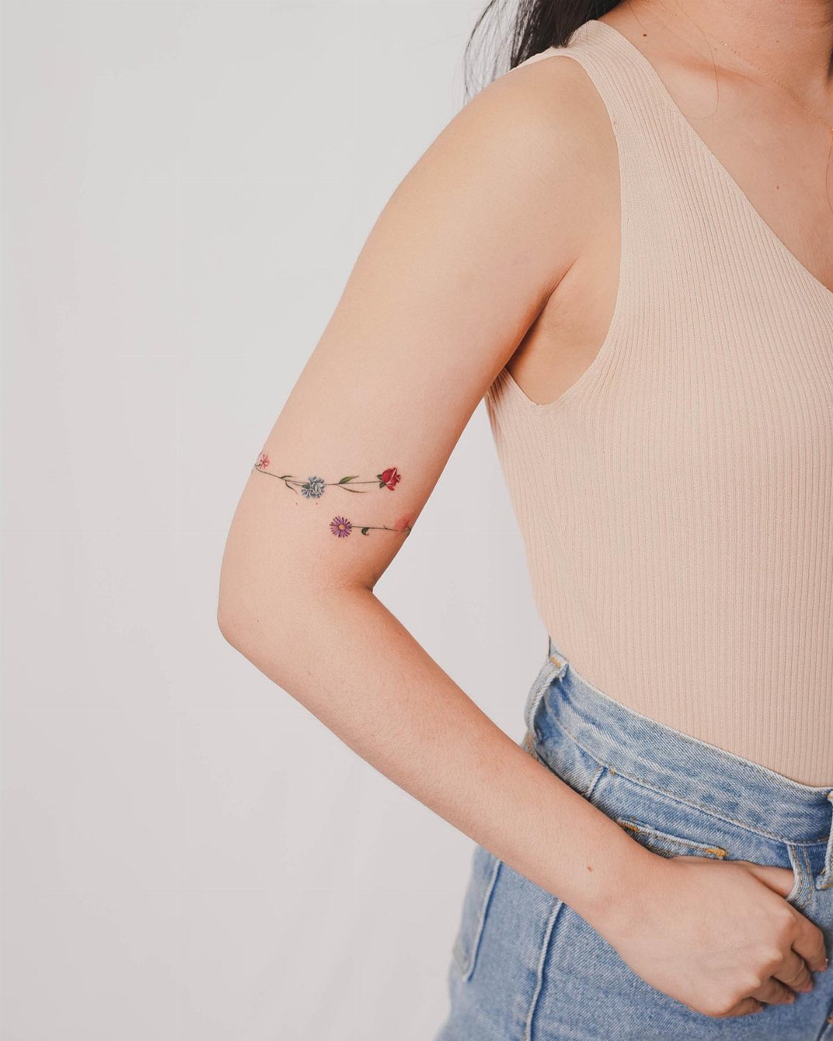 Small colorful flower tattoo wrapping around a person's forearm against a white background