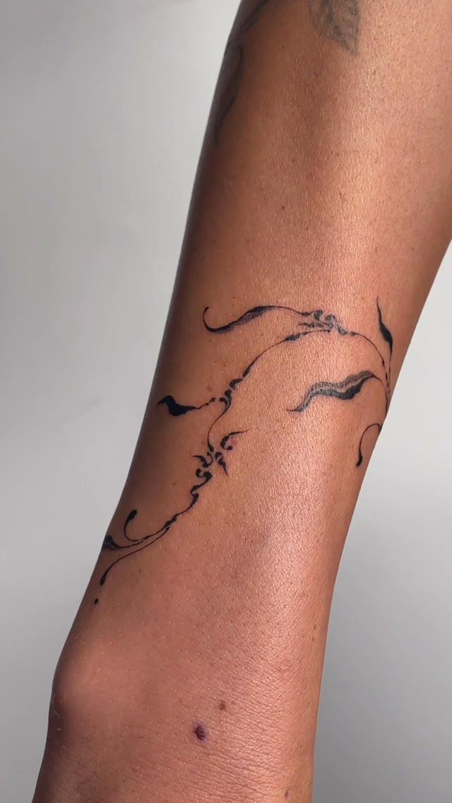 Abstract flowing black ink tattoo on a person's forearm with organic thin lines.