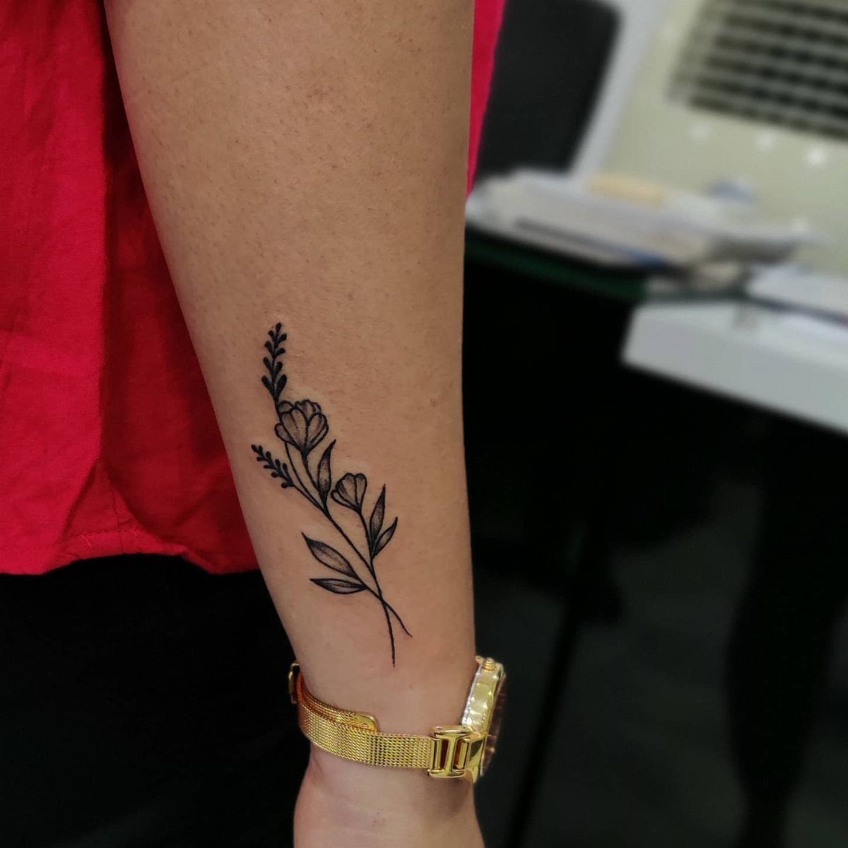 Floral stem tattoo with small flowers and leaves on a person's inner forearm.