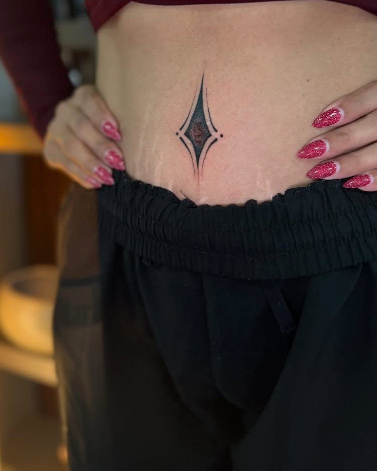 Geometric diamond tattoo on a person's lower abdomen with red glittery nails