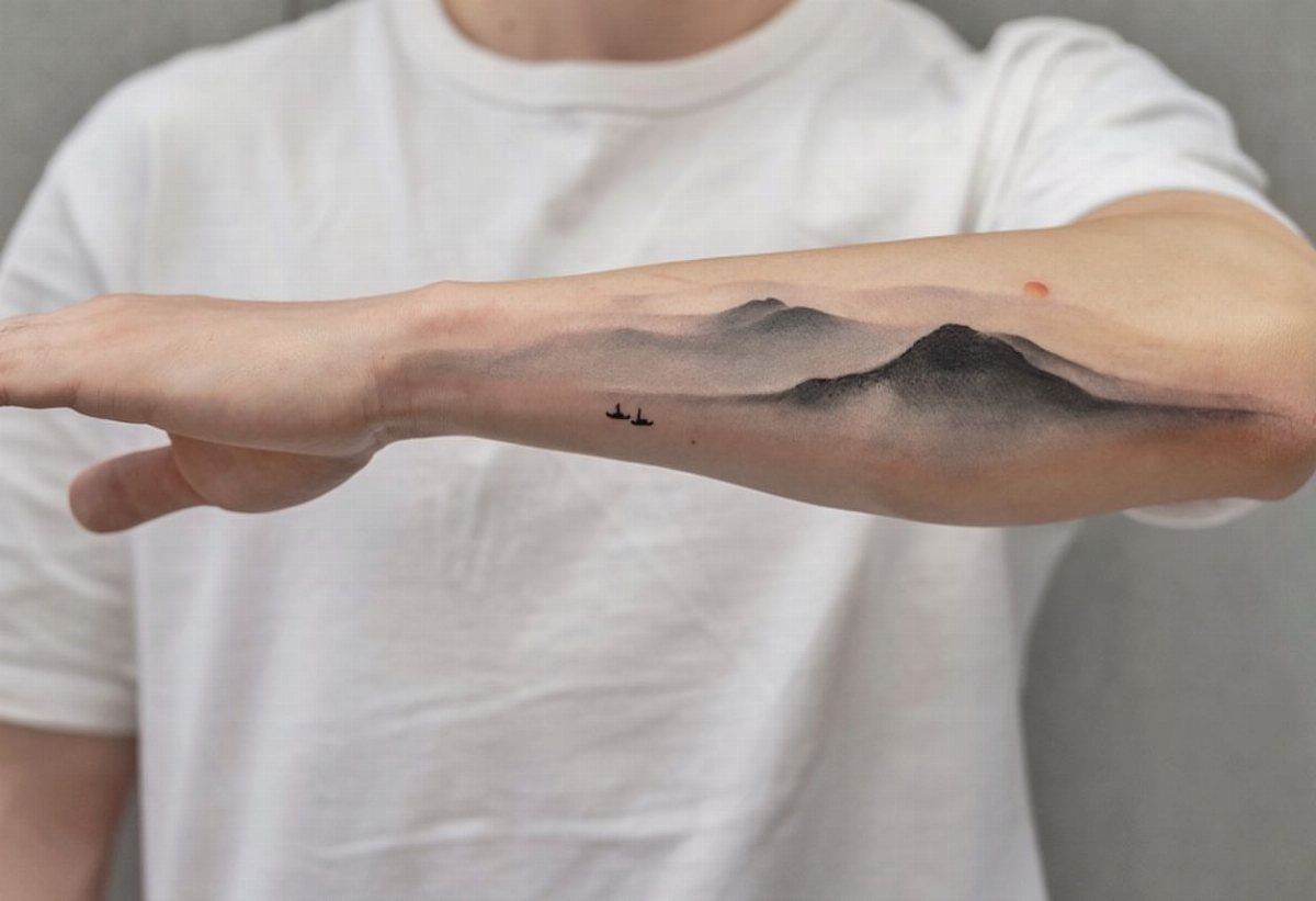 Minimalist mountain landscape tattoo with birds on a person's inner forearm.