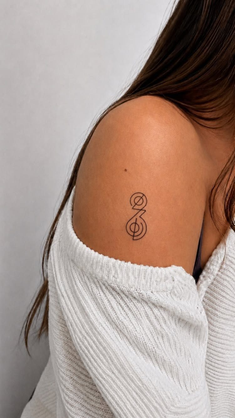 Small black minimalist symbol tattoo on a person's upper arm and shoulder