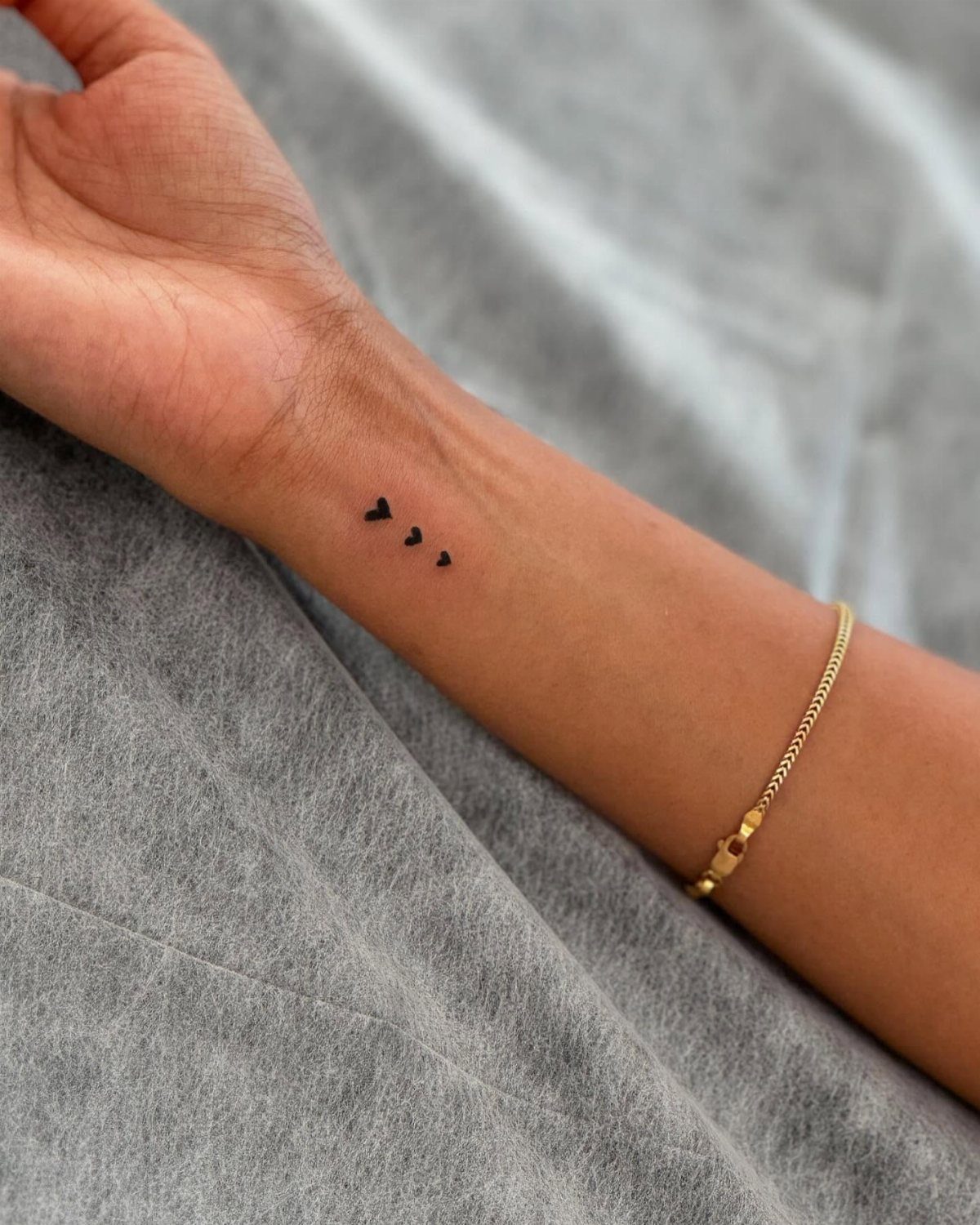 Three tiny black heart tattoos in a row on a person's inner wrist.