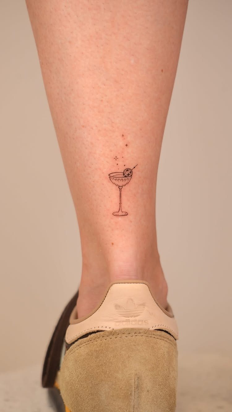 Small martini glass fine line tattoo on a person's ankle above a sneaker