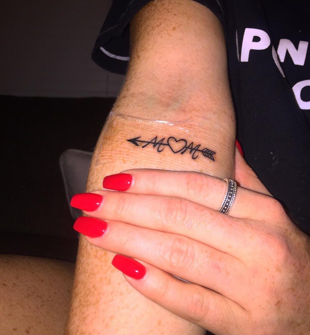 Wrist tattoo of a heart with MOM inside and an arrow through it