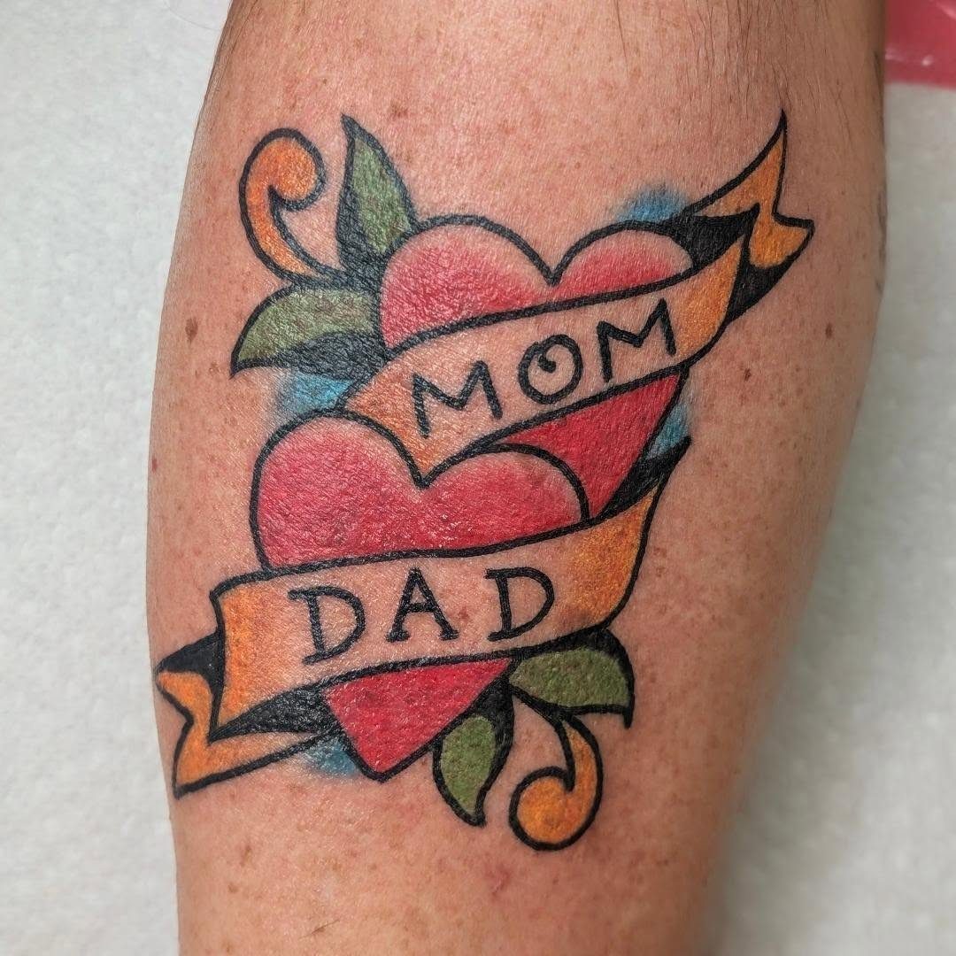 Two red hearts tattoo with banners reading MOM and DAD on skin