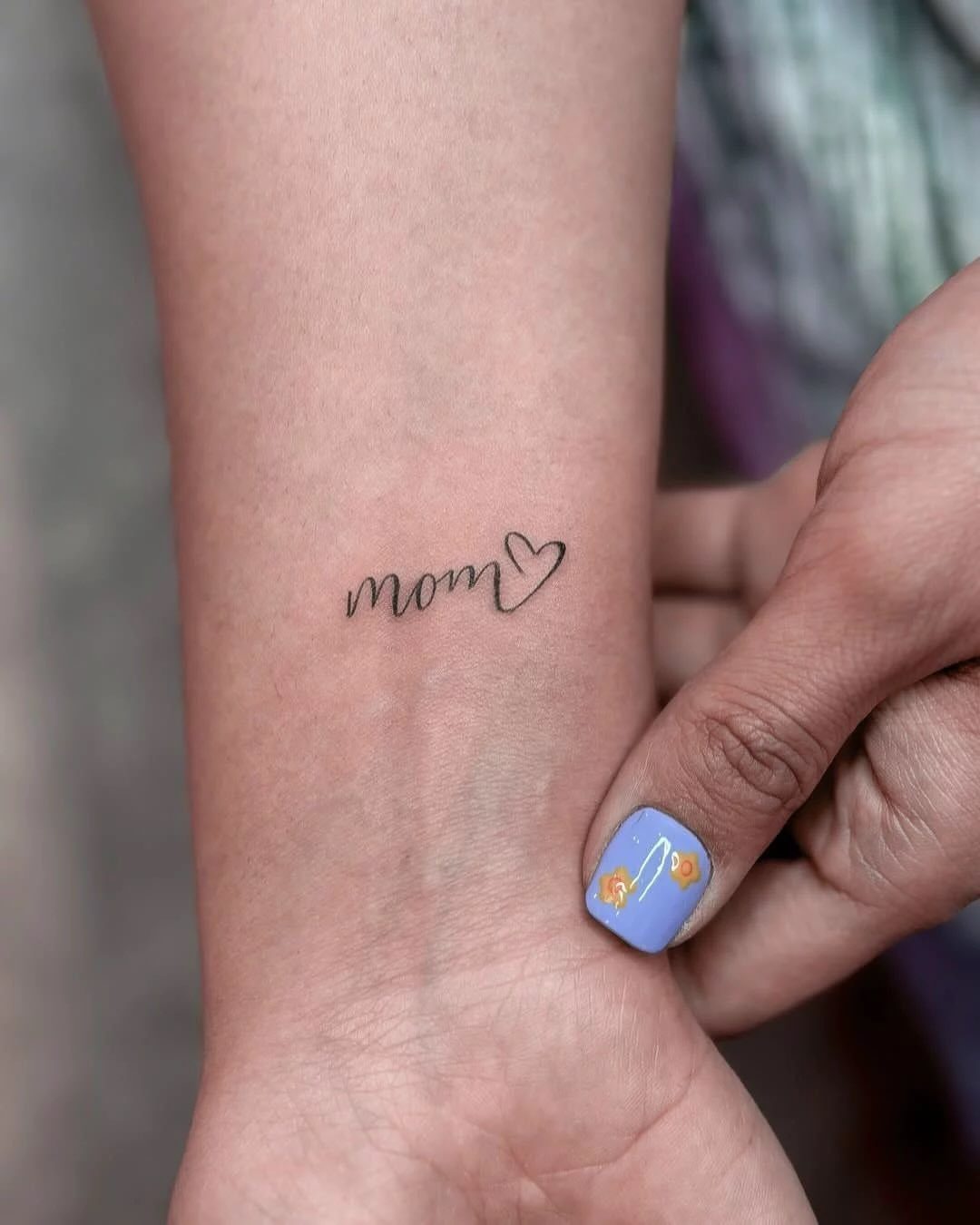 Small black cursive mom heart tattoo on a person's inner wrist