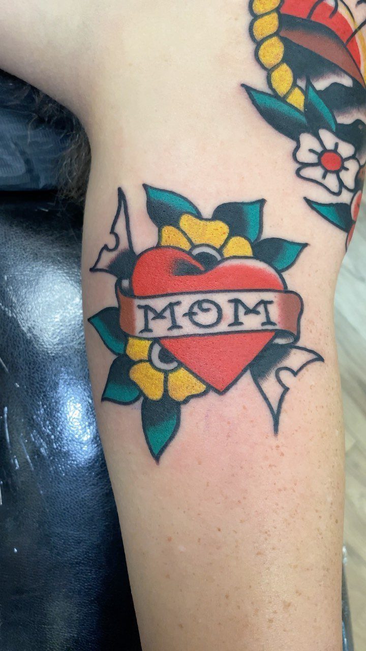 Red heart tattoo with Mom banner and yellow flowers on a person's arm