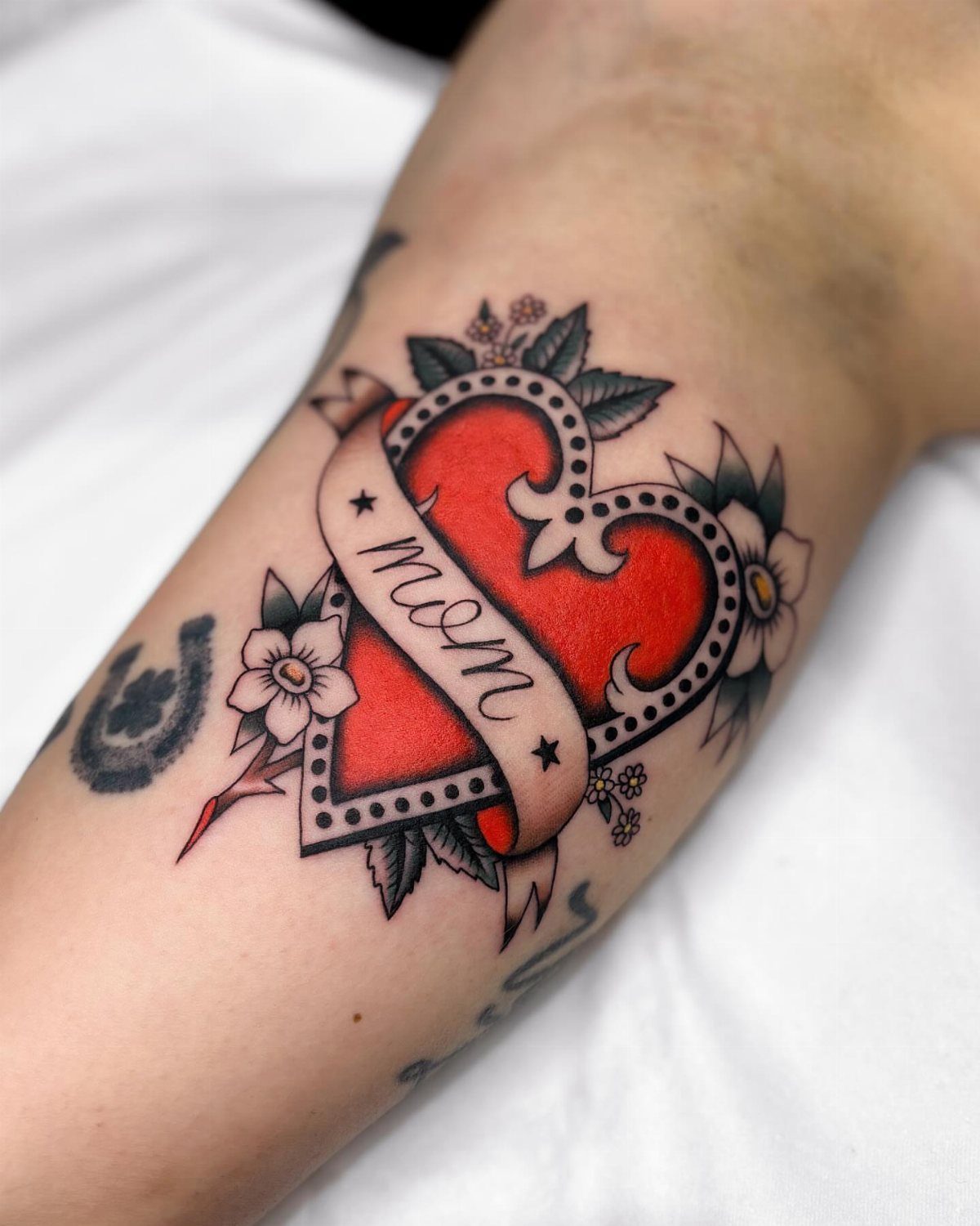 Red heart tattoo with a mom banner and floral accents on skin