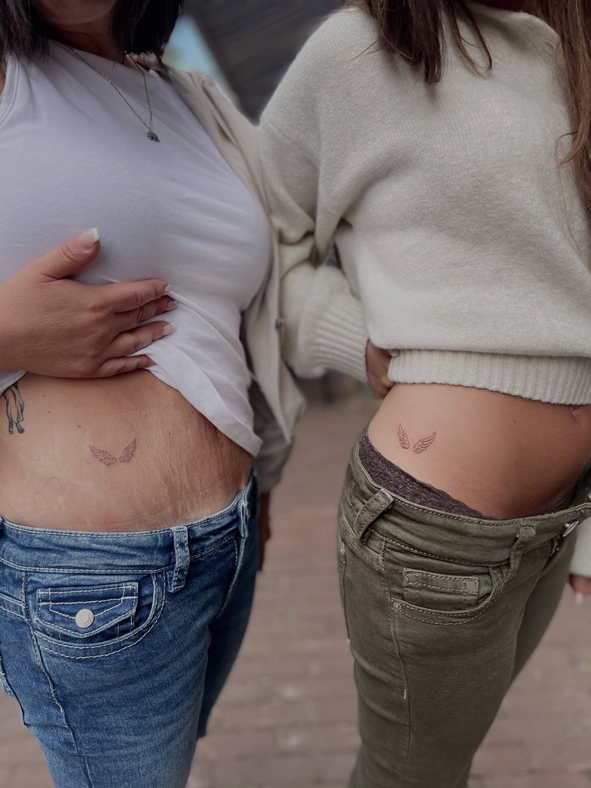 Two women showing matching small angel wing tattoos on their lower hips.
