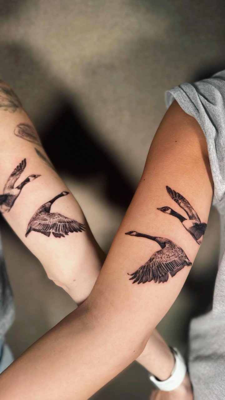 Two matching bird tattoos on the forearms of two people crossing arms.