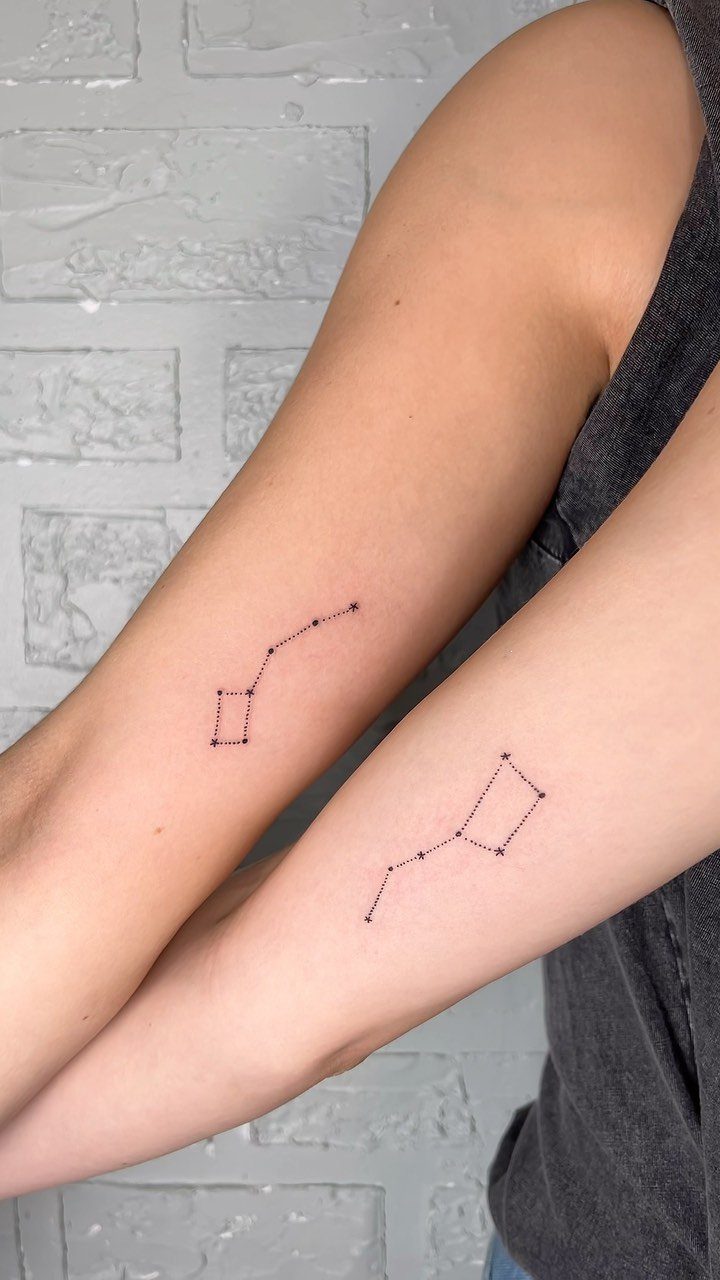 Matching constellation tattoos on the inner forearms of two people against brick wall