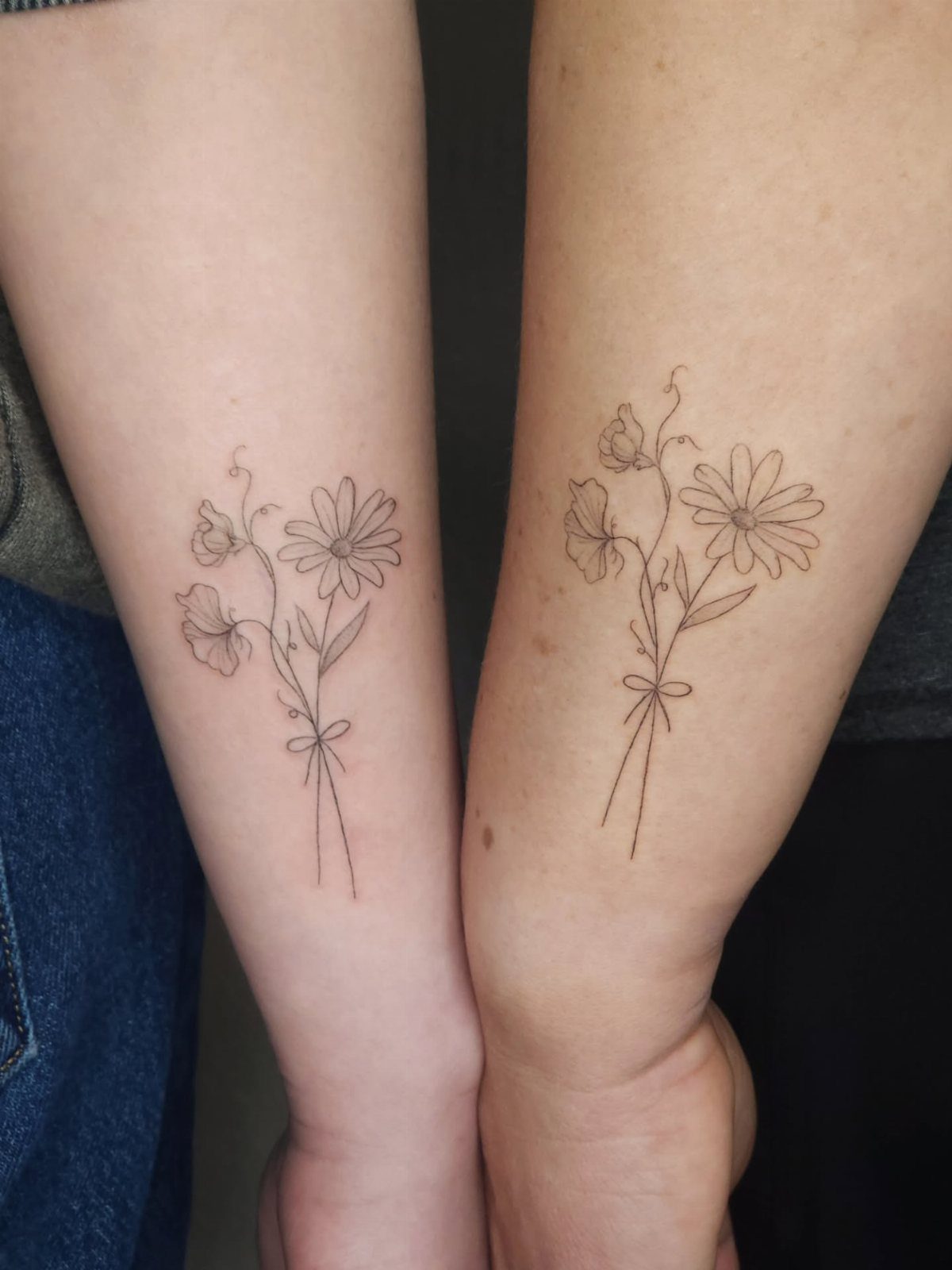 Matching fine-line tattoos of daisy bouquets on two people's inner forearms.