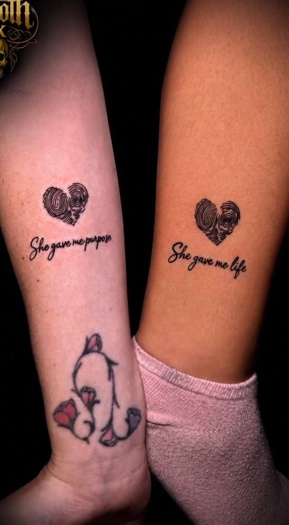 Two arms with matching fingerprint heart tattoos and complementary cursive quotes.