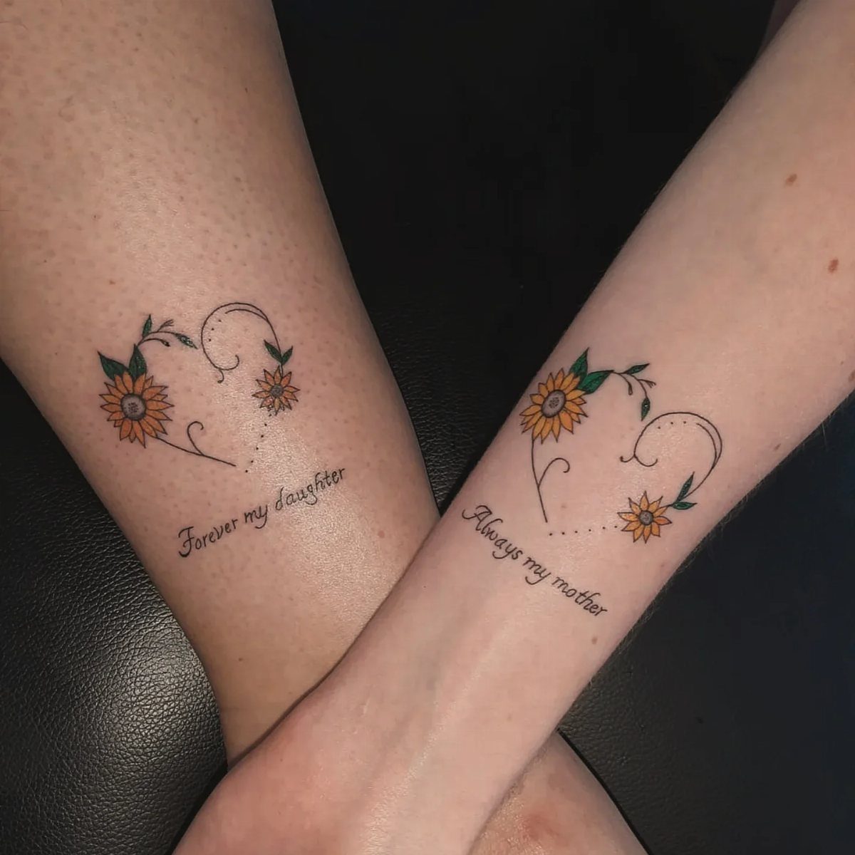 Matching sunflower heart tattoos on two forearms with mother and daughter inscriptions.