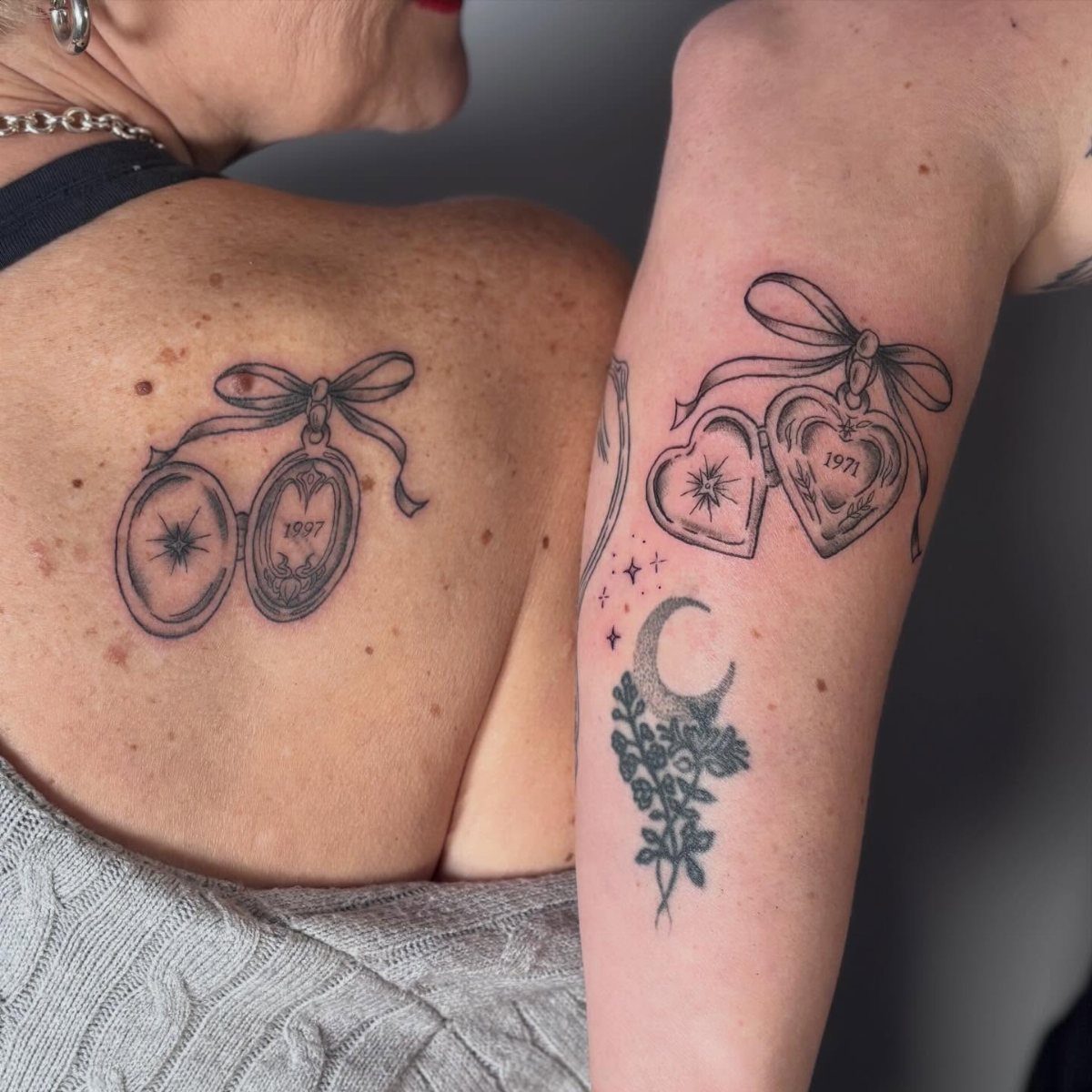 Matching heart locket tattoos on a shoulder and arm with birth years.