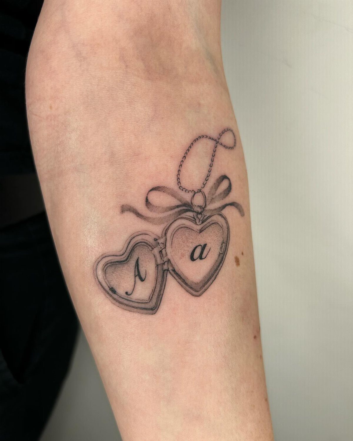 Heart-shaped locket tattoo on an arm with initials A and a.