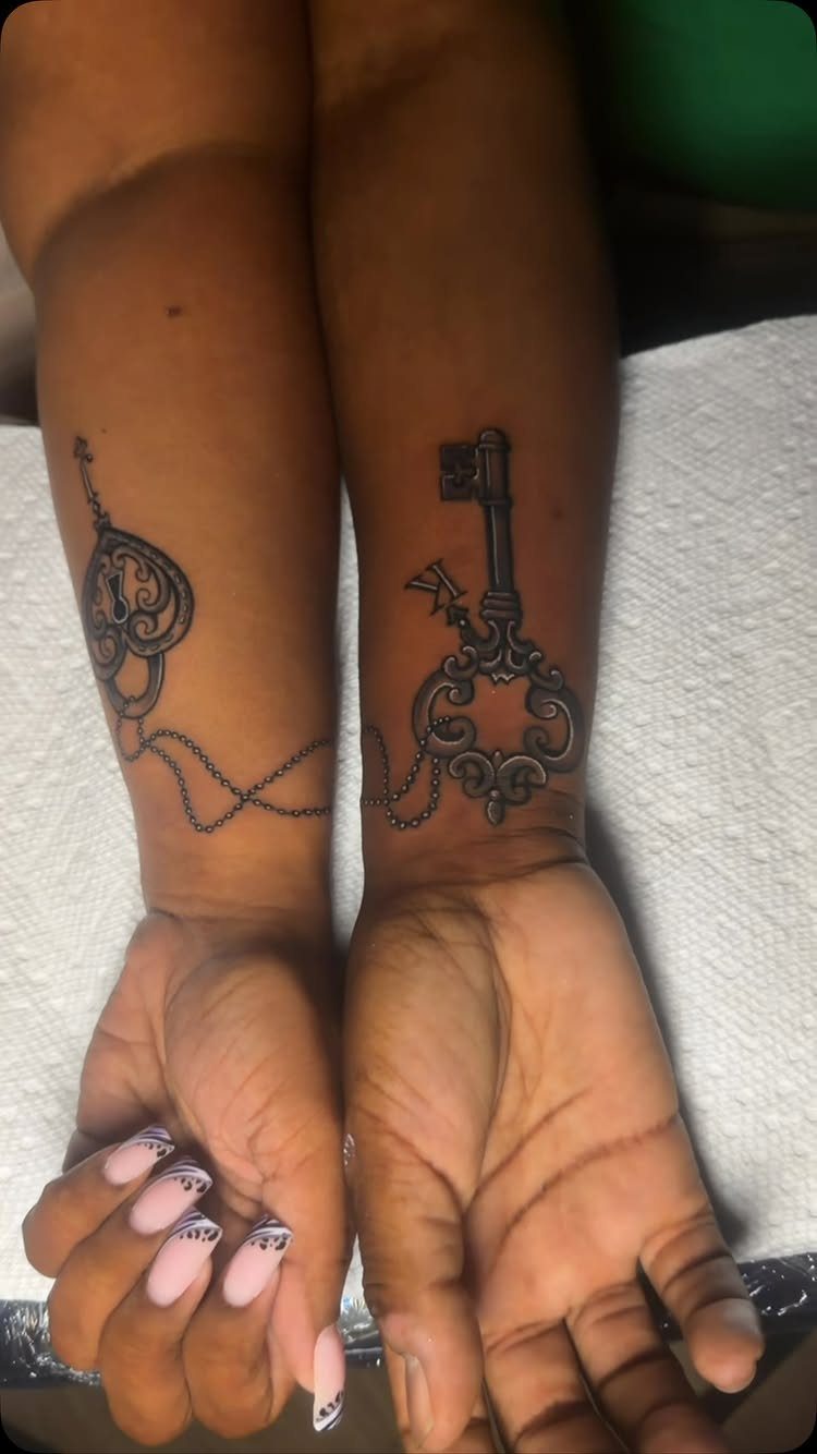 Matching lock and key tattoos on the wrists of two people side-by-side.