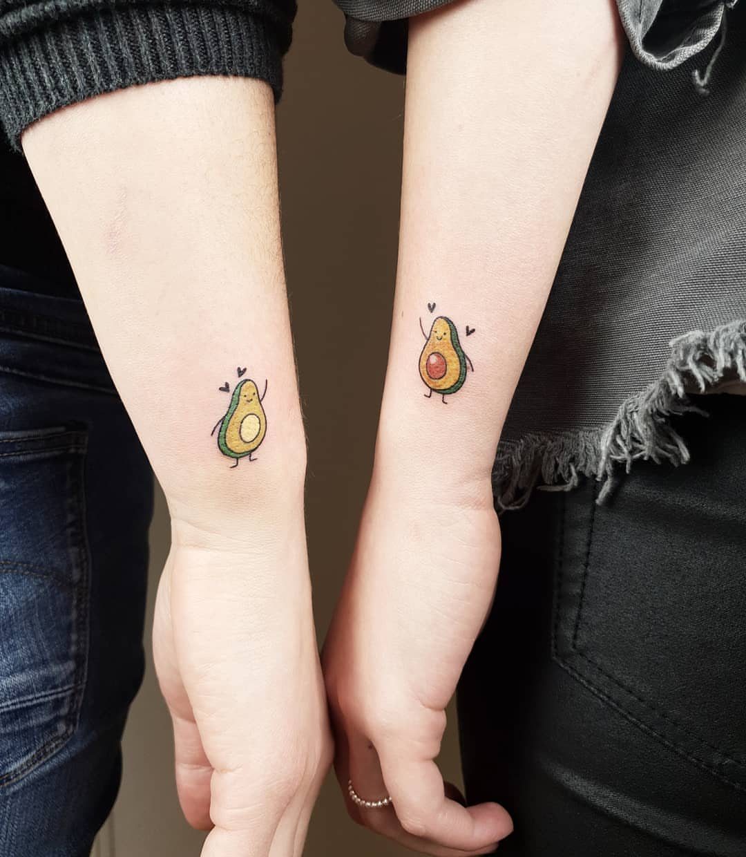 Two inner wrists with matching small avocado half tattoos with cute faces.