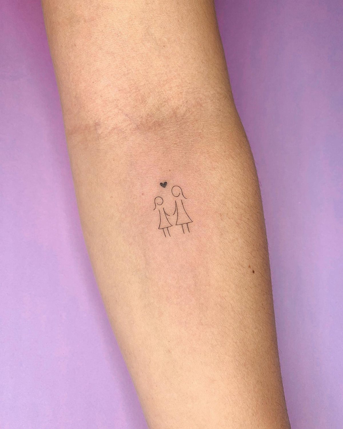 Small black ink tattoo of two female figures holding hands with a heart above.