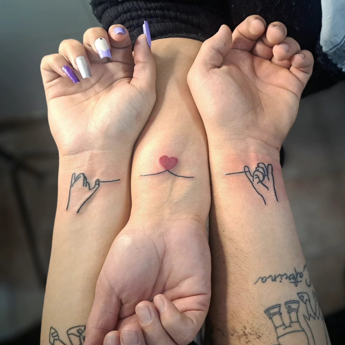 Three wrists with matching pinky promise and heart tattoos forming a connected line.